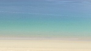 Una playa con agua cristalina y una montaña distante.