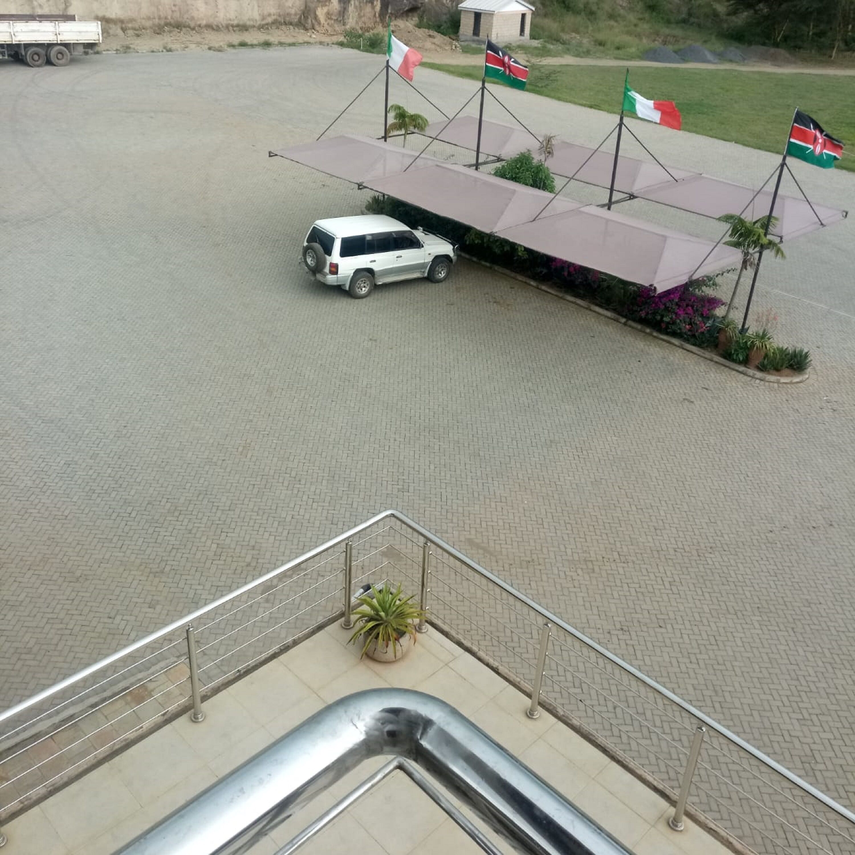 A parking area with a white SUV, a covered waiting area with flags, and a staircase leading to a lower level.