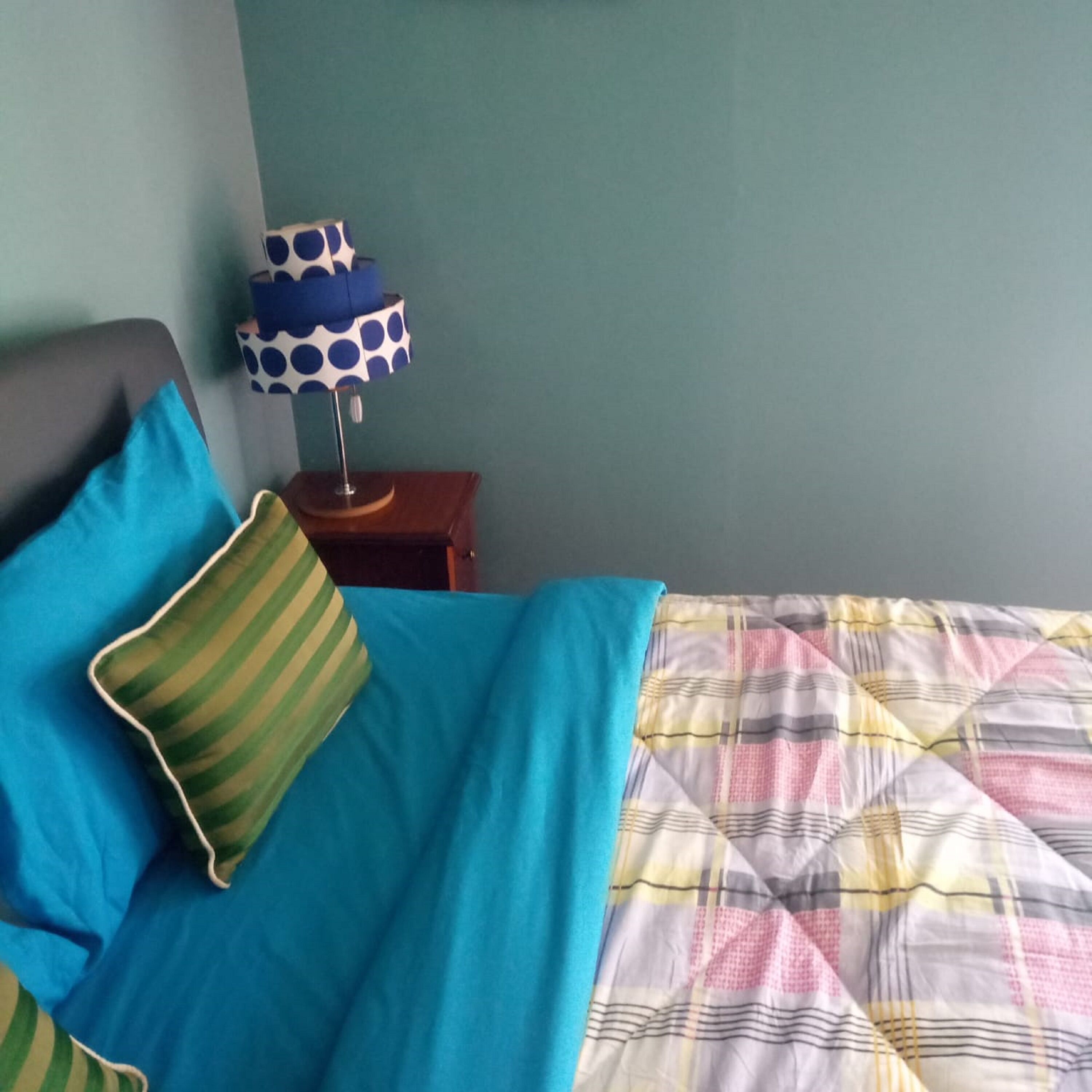 A bed with a blue and green striped pillow, a quilted bedspread, and a blue polka dot lamp on a wooden nightstand.