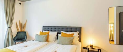 A modern hotel room with a large bed, a nightstand, a chair, and a mirror on the wall.