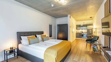 A modern hotel room with a large bed, a bedside table, a chair, and a small desk with a computer.