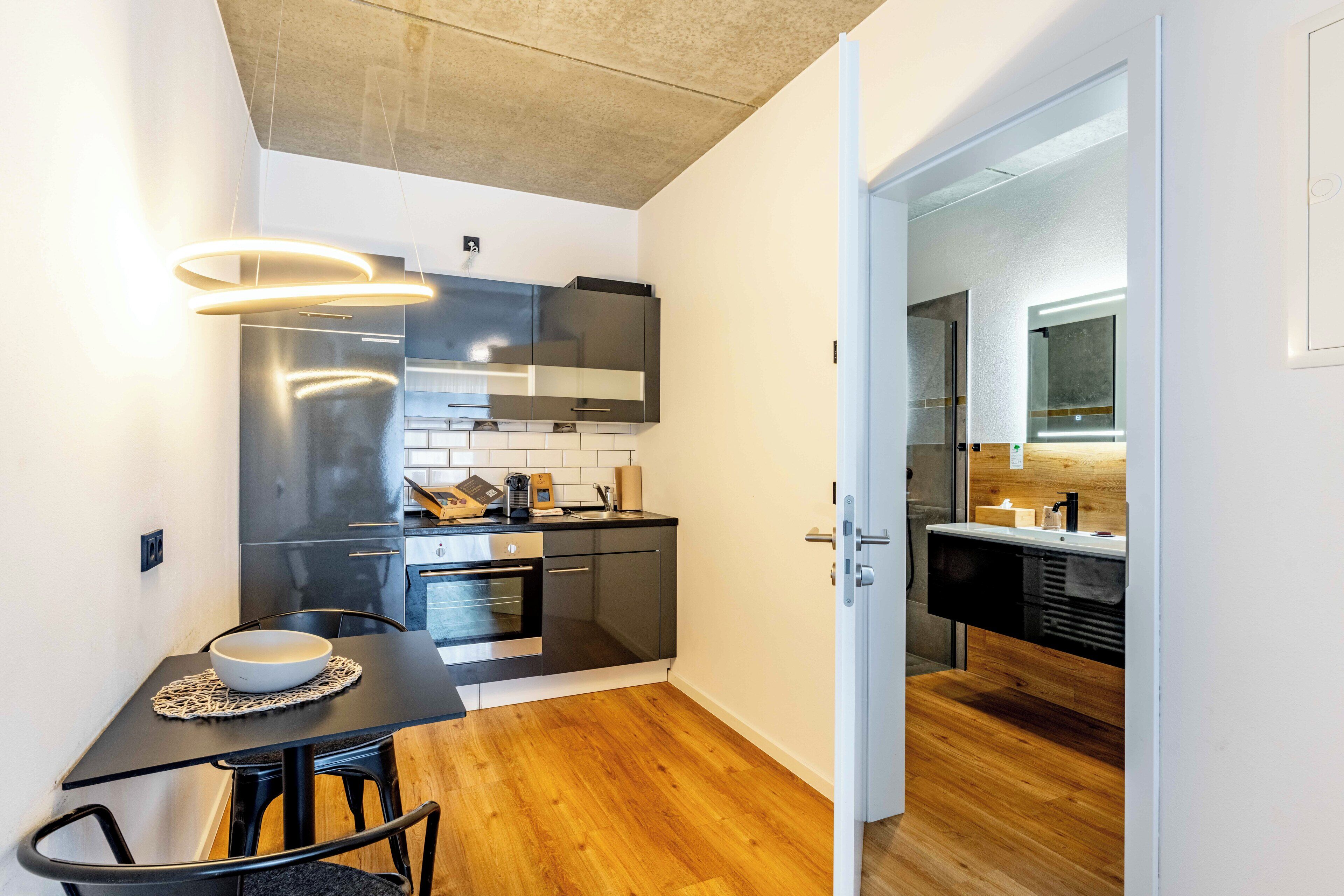A modern kitchen with a dining area, featuring a wooden floor, black and white cabinetry, and a built-in oven.