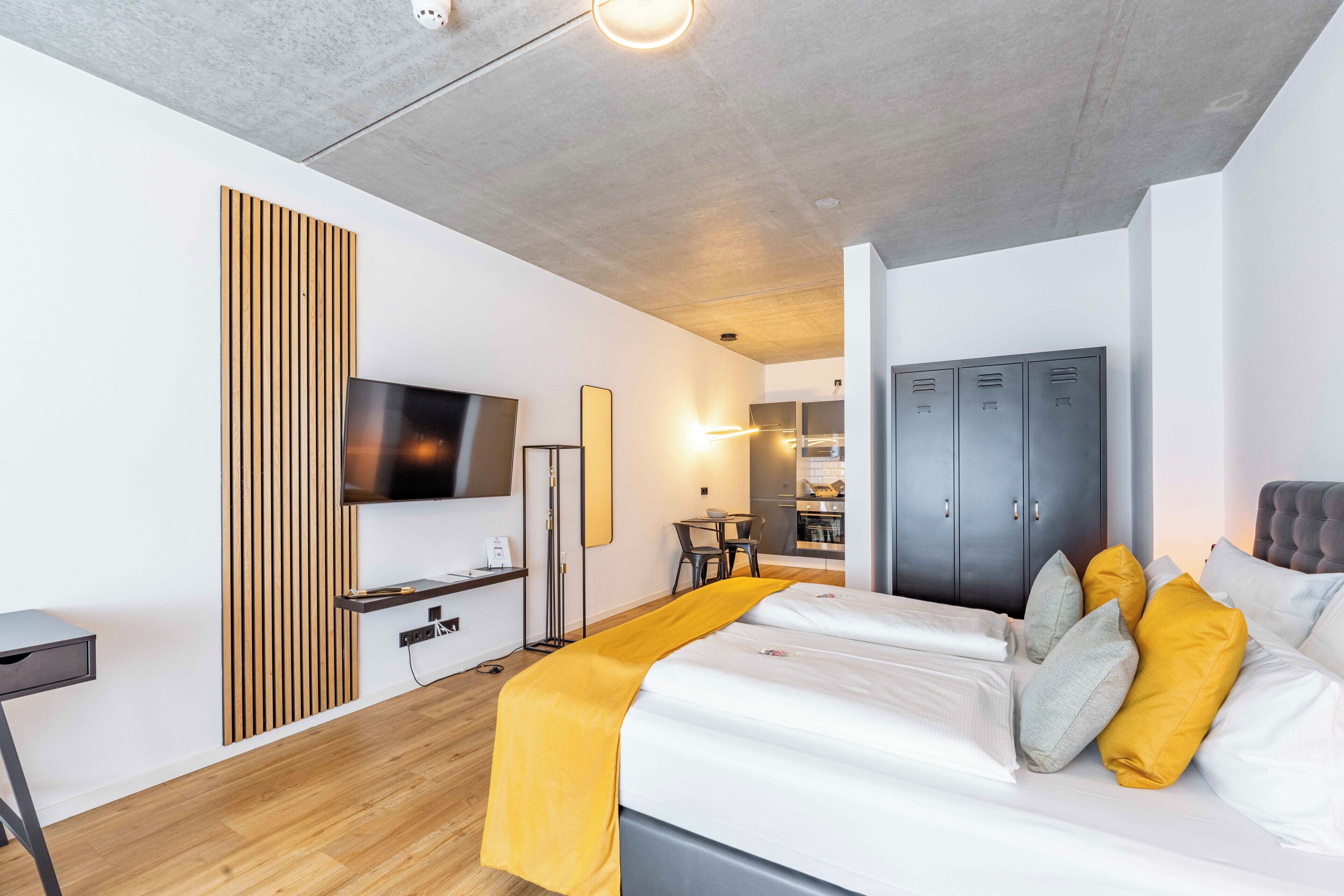 Een moderne hotelkamer met een groot bed, een aan de muur bevestigde televisie, een houten paneel, een bureau en een kledingkast.