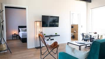 A modern hotel room with a bed, a TV, a desk, and a dining area.
