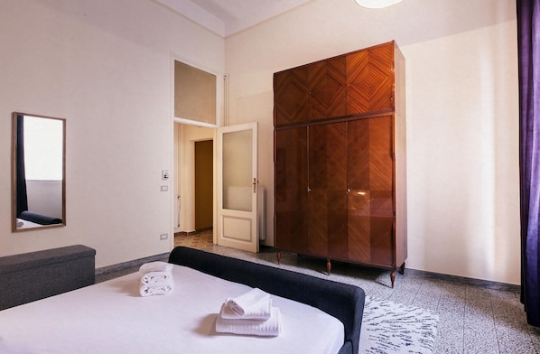 A hotel room with a bed, a large wardrobe, a mirror, and a door leading to another room.