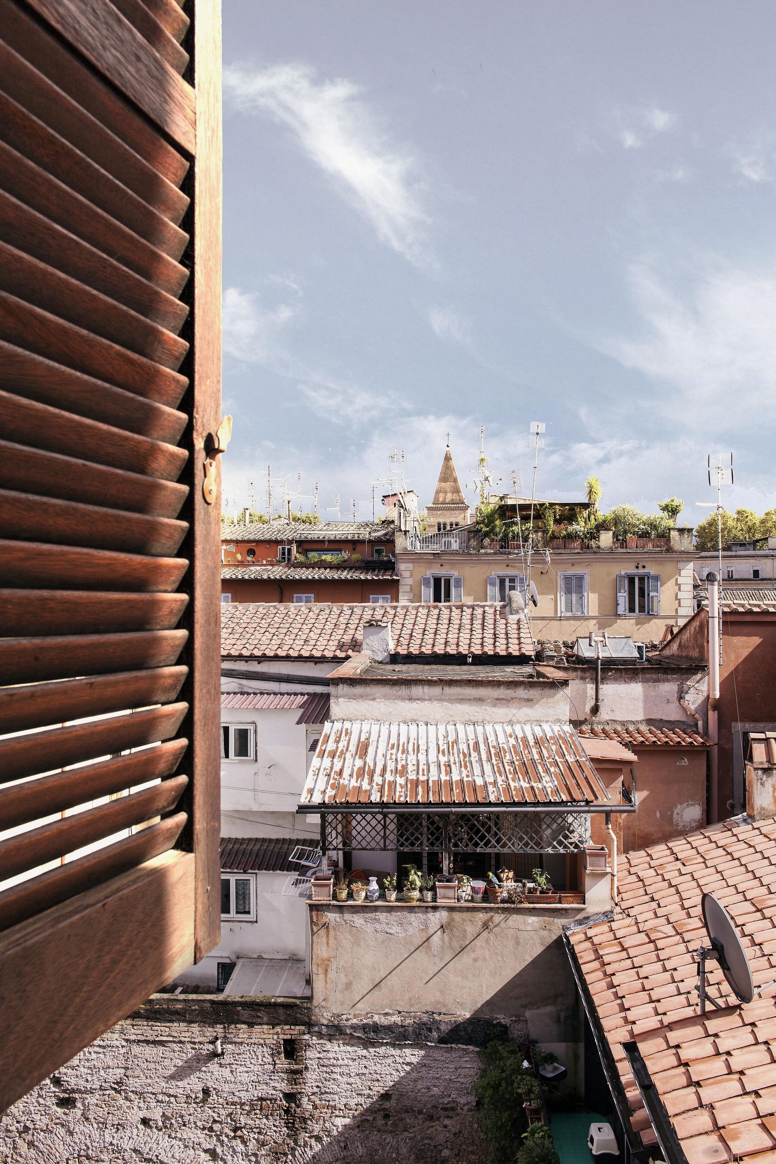 A view from a window overlooking a cityscape with terracotta rooftops, a prominent church with a dome, and a clear sky.