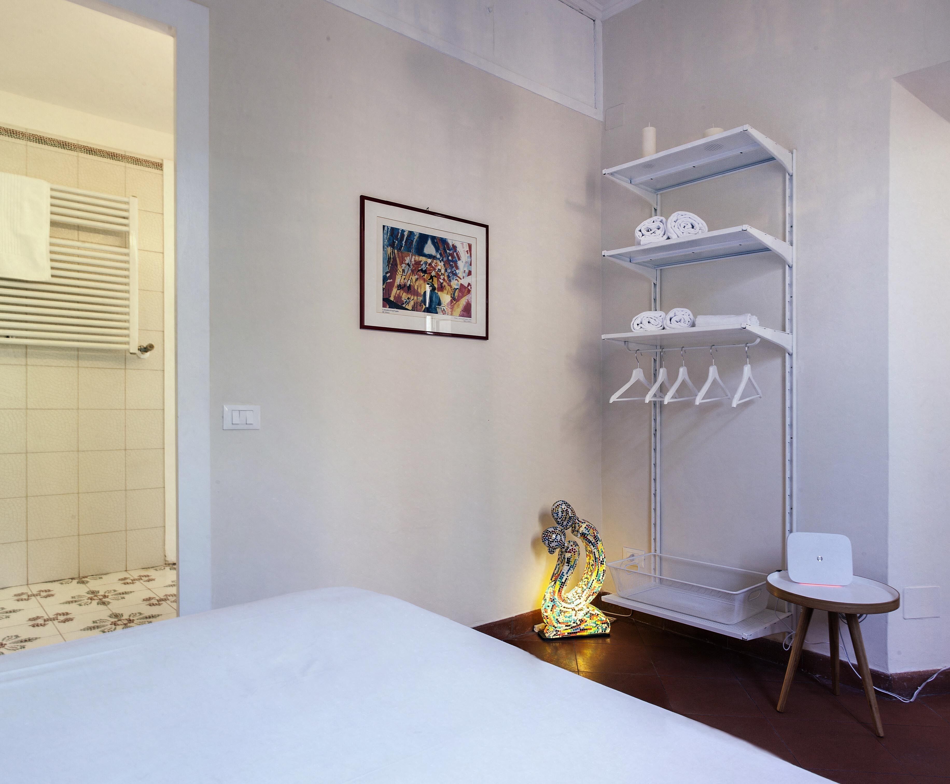 Habitación de hotel con cama, estante con toallas, un cuadro enmarco y una lámpara decorativa.