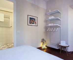 Habitación de hotel con cama, estante con toallas, un cuadro enmarco y una lámpara decorativa.