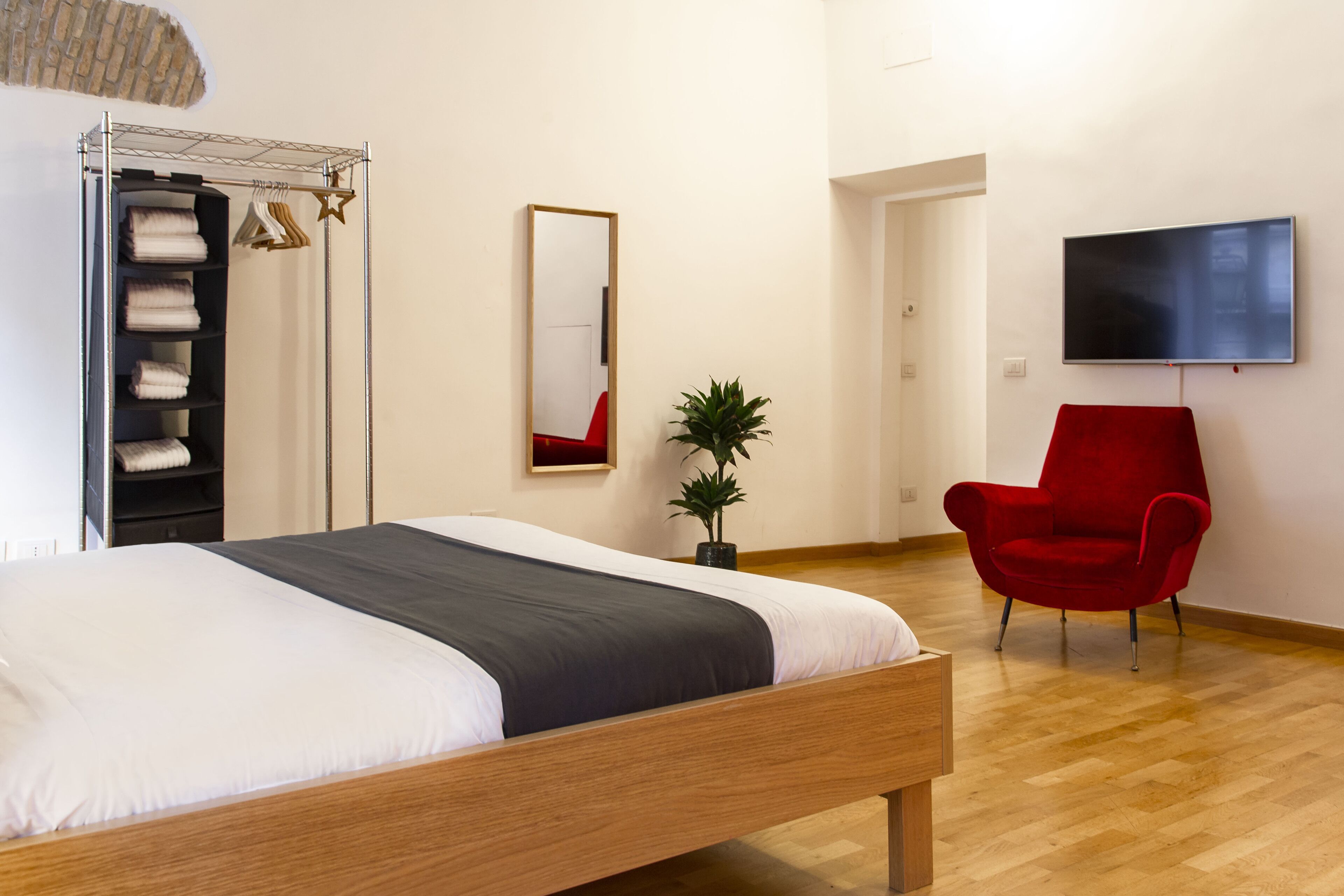 A bedroom with a wooden bed, a red chair, a TV, a mirror, and a plant.