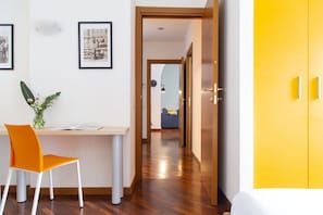 Una habitación moderna con piso de madera, un escritorio con silla, un armario amarillo y cuadros enmarcados en la pared.