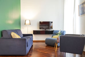 Una sala moderna con una televisión de pantalla plana, dos sofás, una mesita auxiliar y una lámpara.
