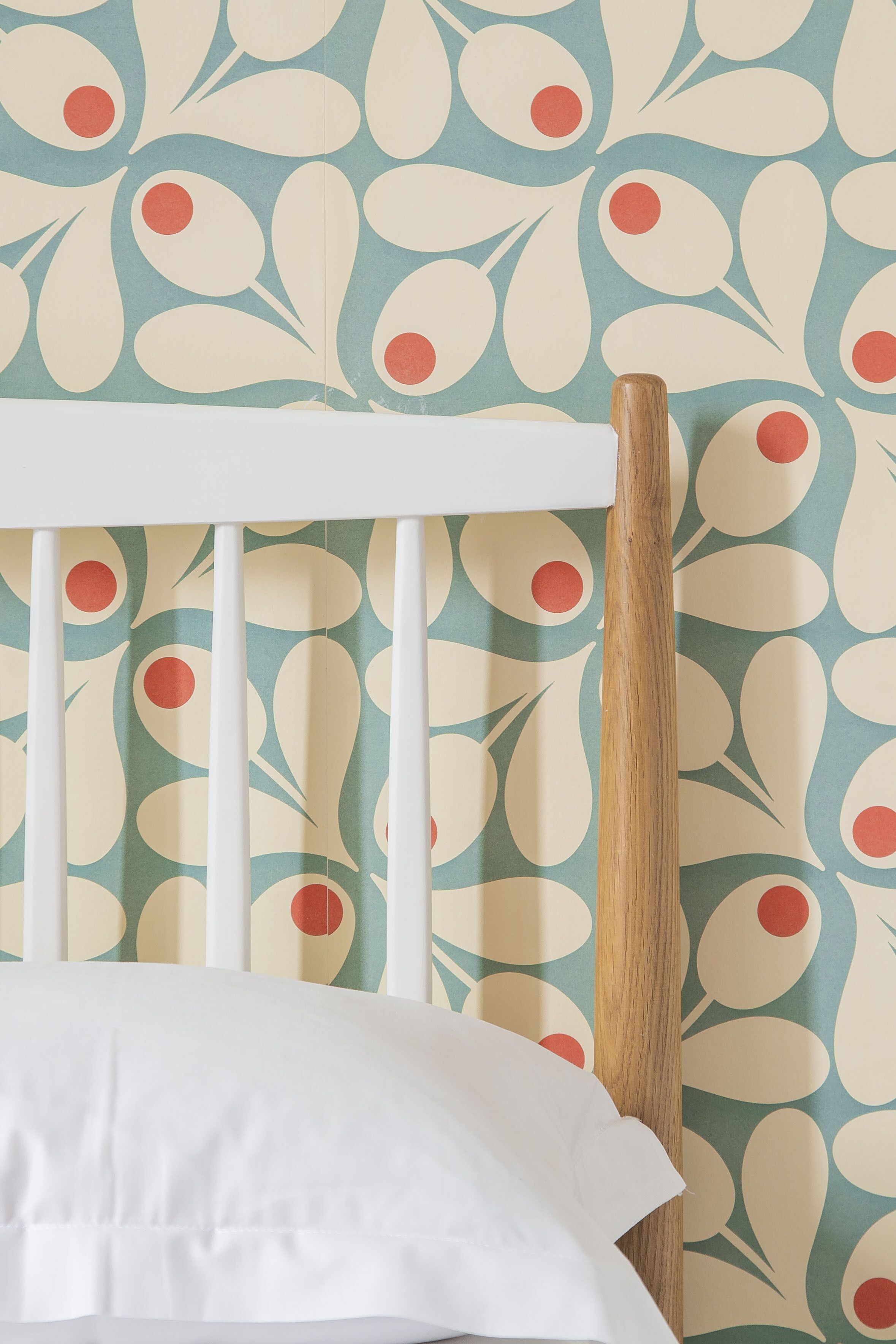 A crib with a white mattress and a wooden post, set against a wall with a leafy pattern.