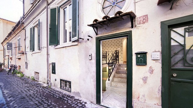 Una estrecha calle adoquinada con un edificio que tiene una puerta verde y una escalera que sube a un piso superior.