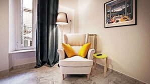 Una habitación con un sillón blanco con cojines amarillos, una lámpara de pie, una pequeña mesa redonda y una obra de arte enmarcada en la pared.