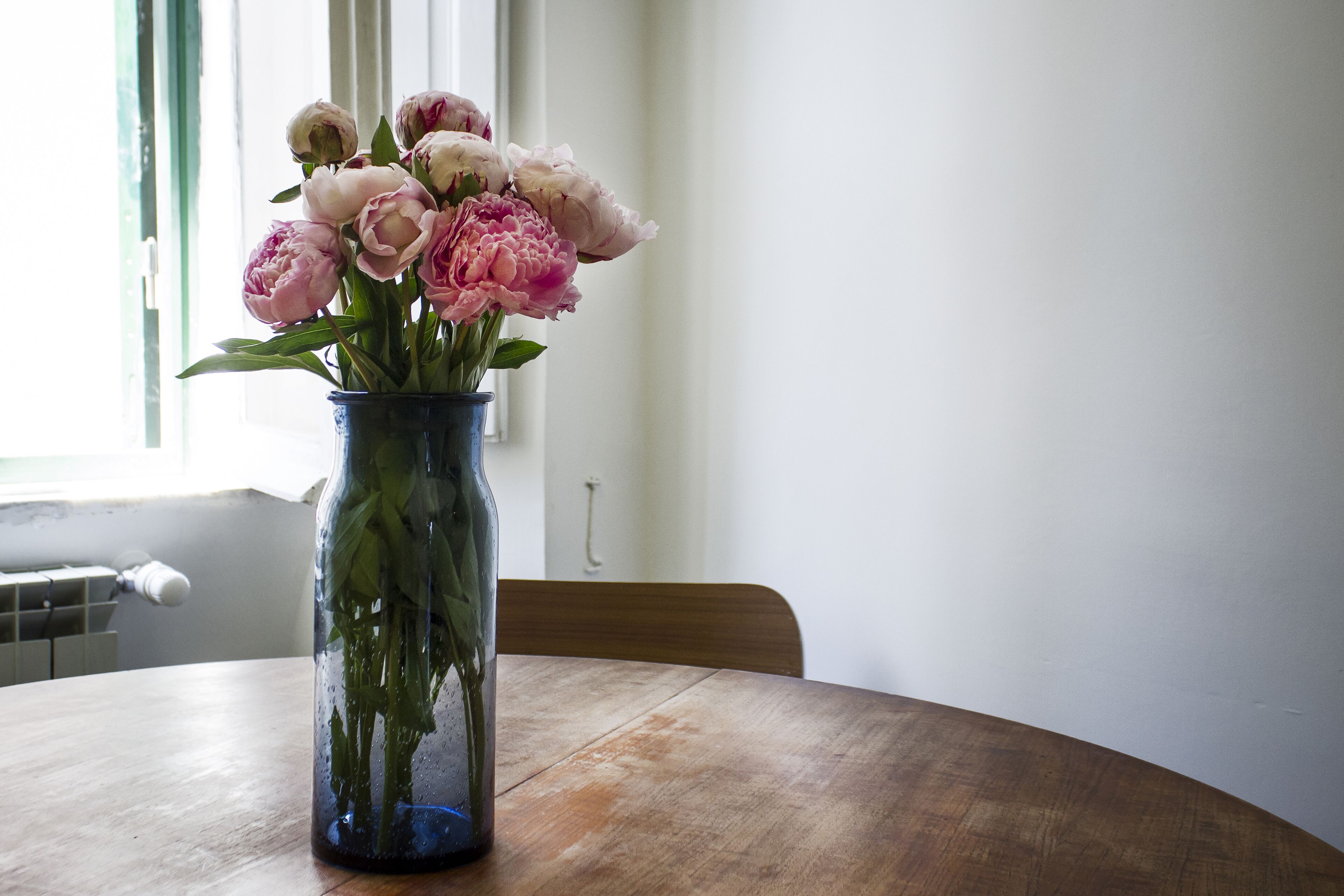 Un jarrón con flores sobre una mesa de madera junto a una ventana.