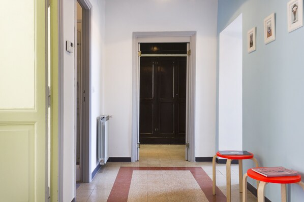 A hallway with a radiator, a door leading to a dark room, and two red stools.