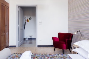 A hotel room with a bed, a red chair, a desk with a lamp, and a view of the hallway. - Cosimato RTH (Rome)