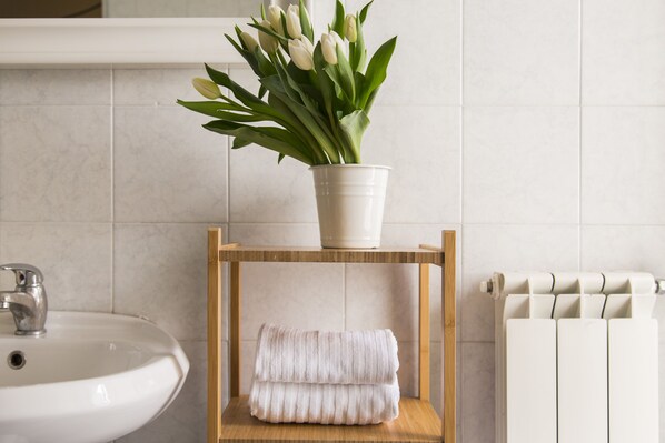 A bathroom with a white sink, a wooden shelf with a white towel, and a potted plant with green leaves and white flowers.