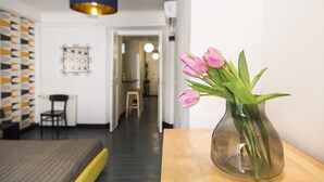 Ein Zimmer mit Holztisch, einer Vase mit rosa Blumen, einer blauen Hängelampe und einer Wand mit Muster.