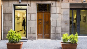 Un edificio con un portal de madera doble, dos plantas en macetas y un suelo adoquinado.