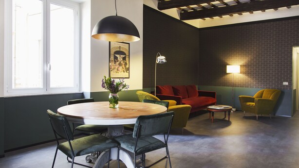 A modern living room with a round wooden table, green and yellow chairs, a red sofa, and a floor lamp. - Genovesi RTH (Rome)