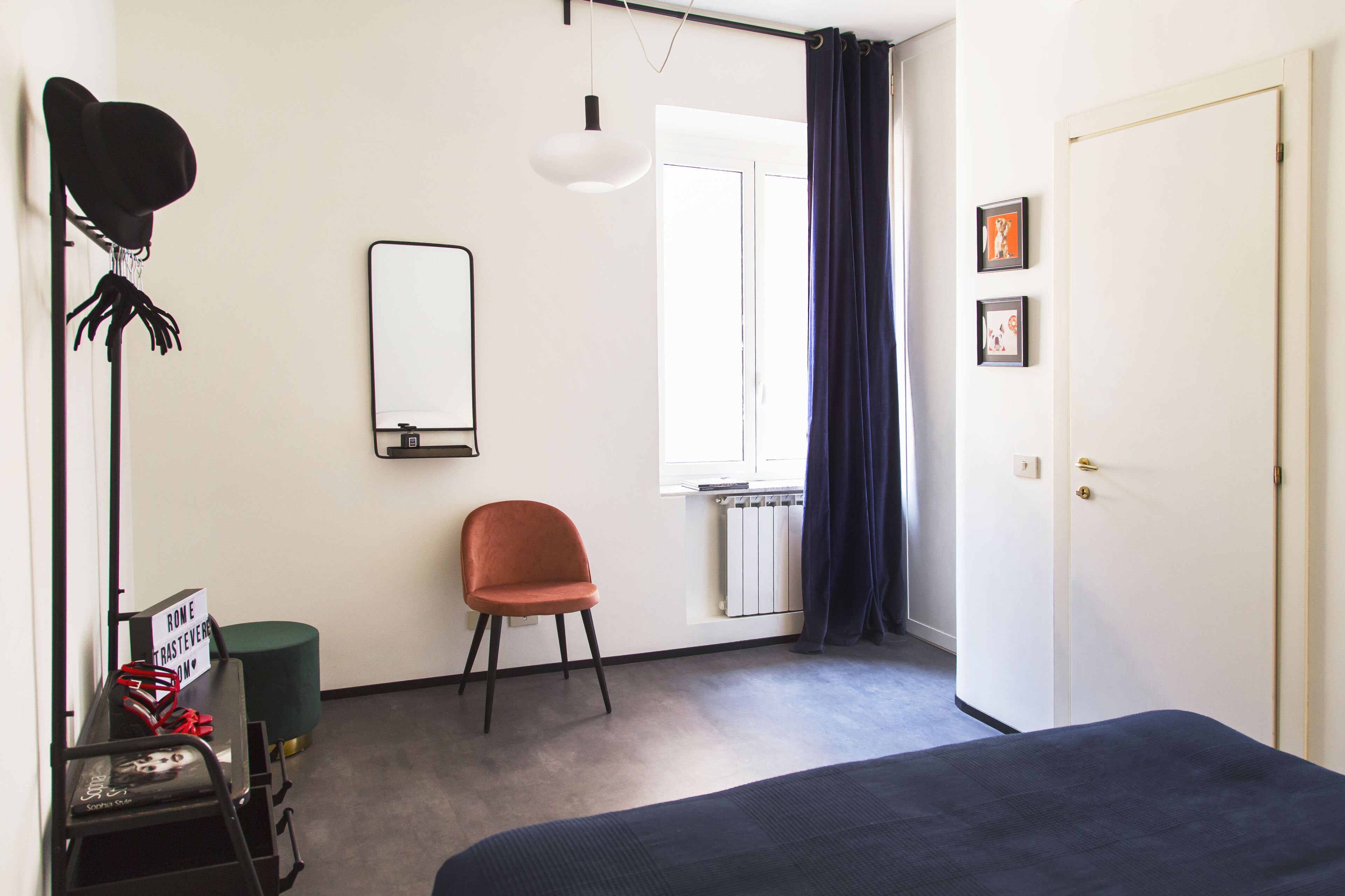 Een slaapkamer met een bed, een stoel, een radiator, een raam met gordijnen, een deur en een spiegel aan de muur.