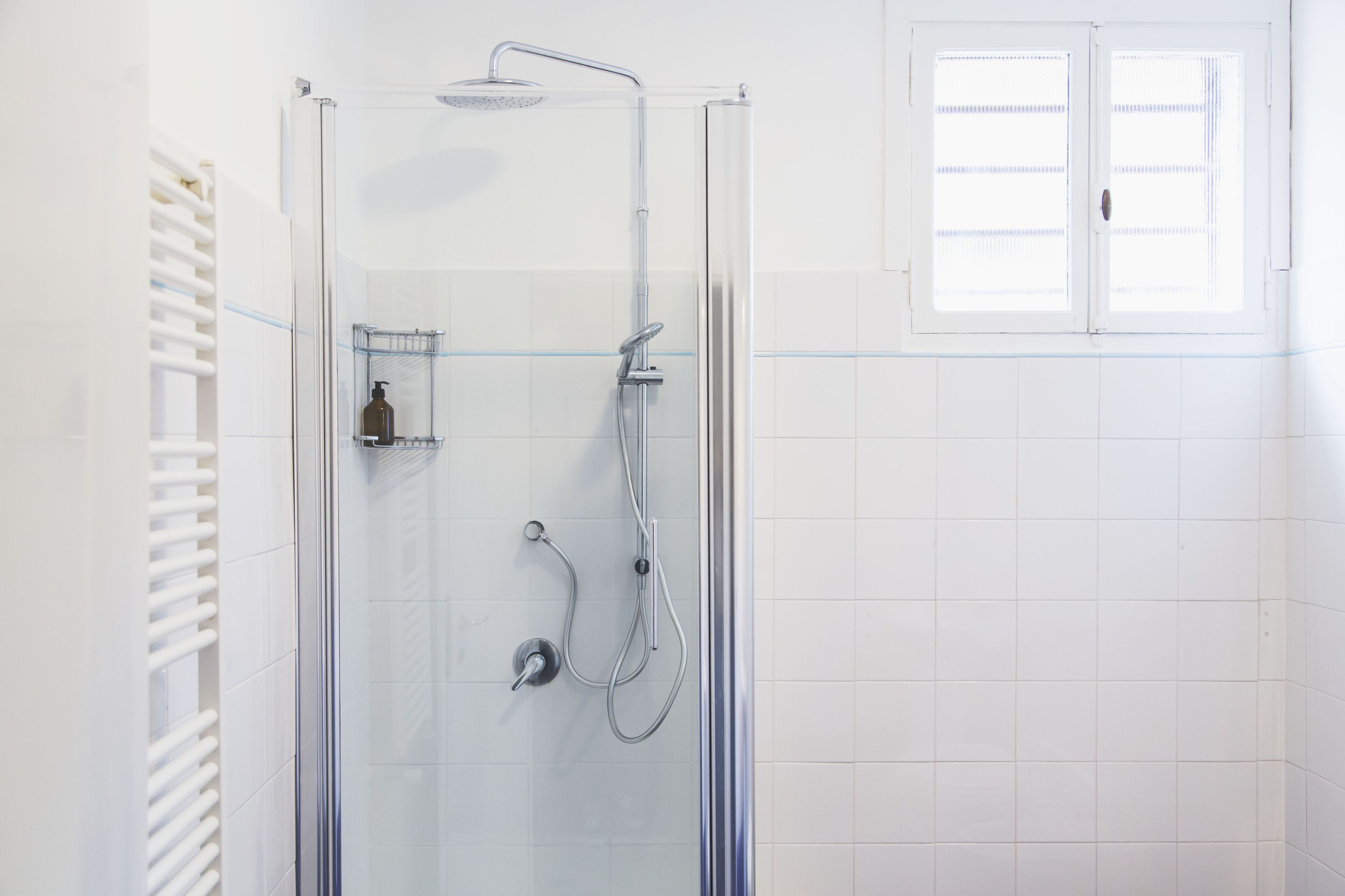 A glass-enclosed shower with a handheld showerhead and a wall-mounted faucet.