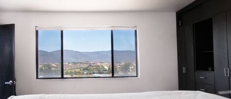 A bedroom with a bed, a ceiling fan, a window with a mountain view, and dark wooden cabinets.