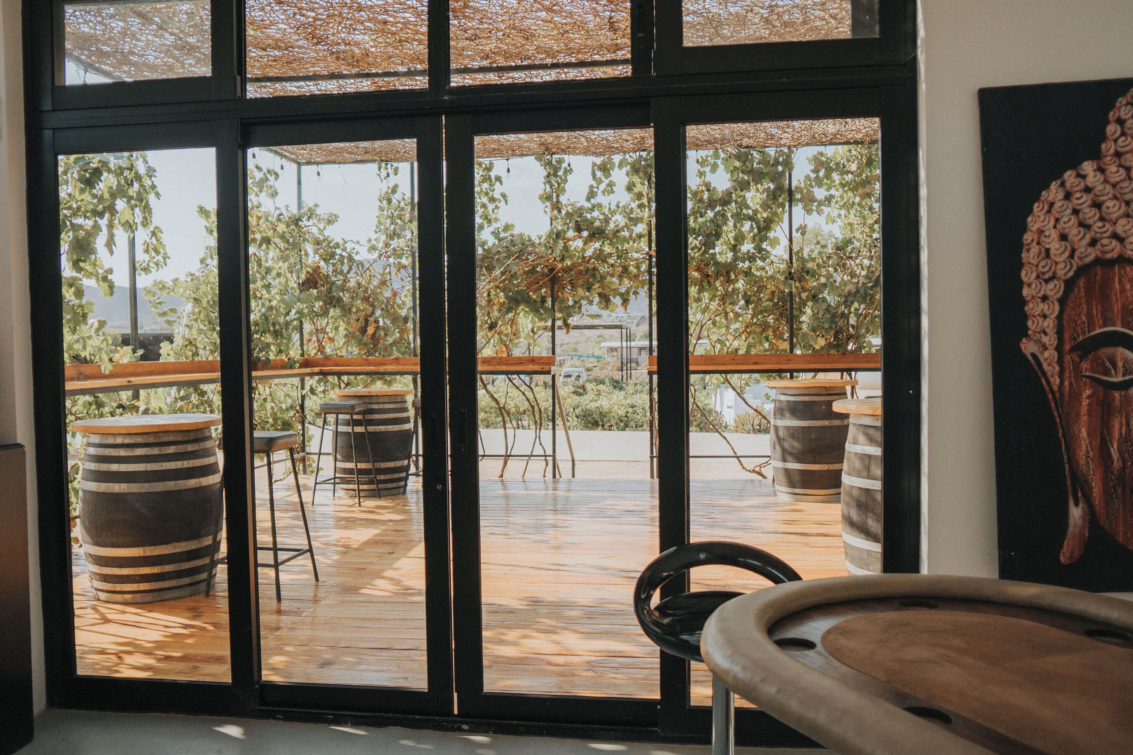 A room with large windows, wooden flooring, and rustic decor including barrels and a wooden bench.