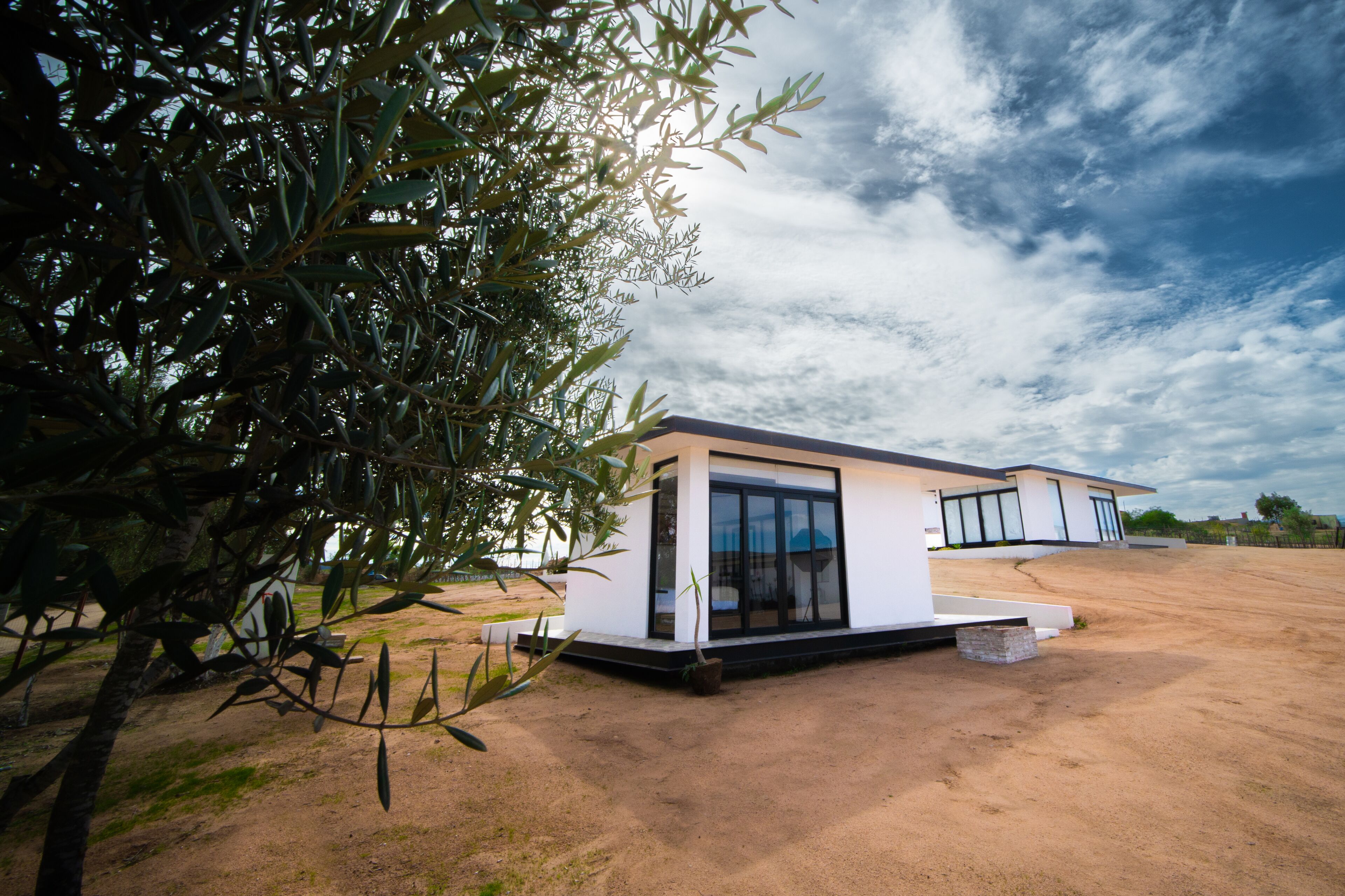 Une maison moderne dotée d’une grande fenêtre, d’un petit porche et d’une cour en terre.