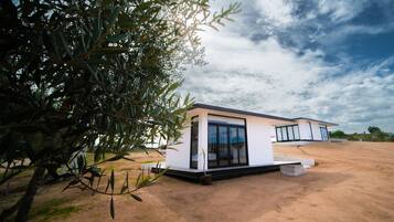 Une maison moderne dotée d’une grande fenêtre, d’un petit porche et d’une cour en terre.