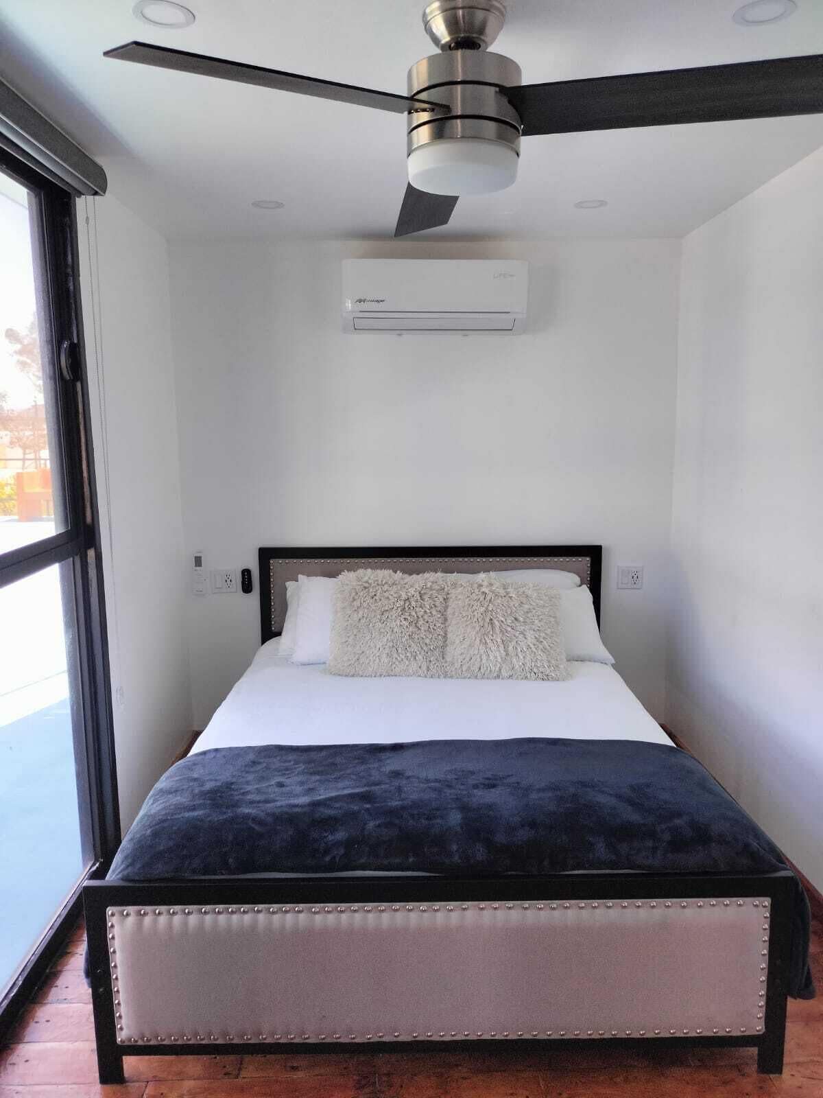 A modern bedroom with a bed, a ceiling fan, and an air conditioning unit.