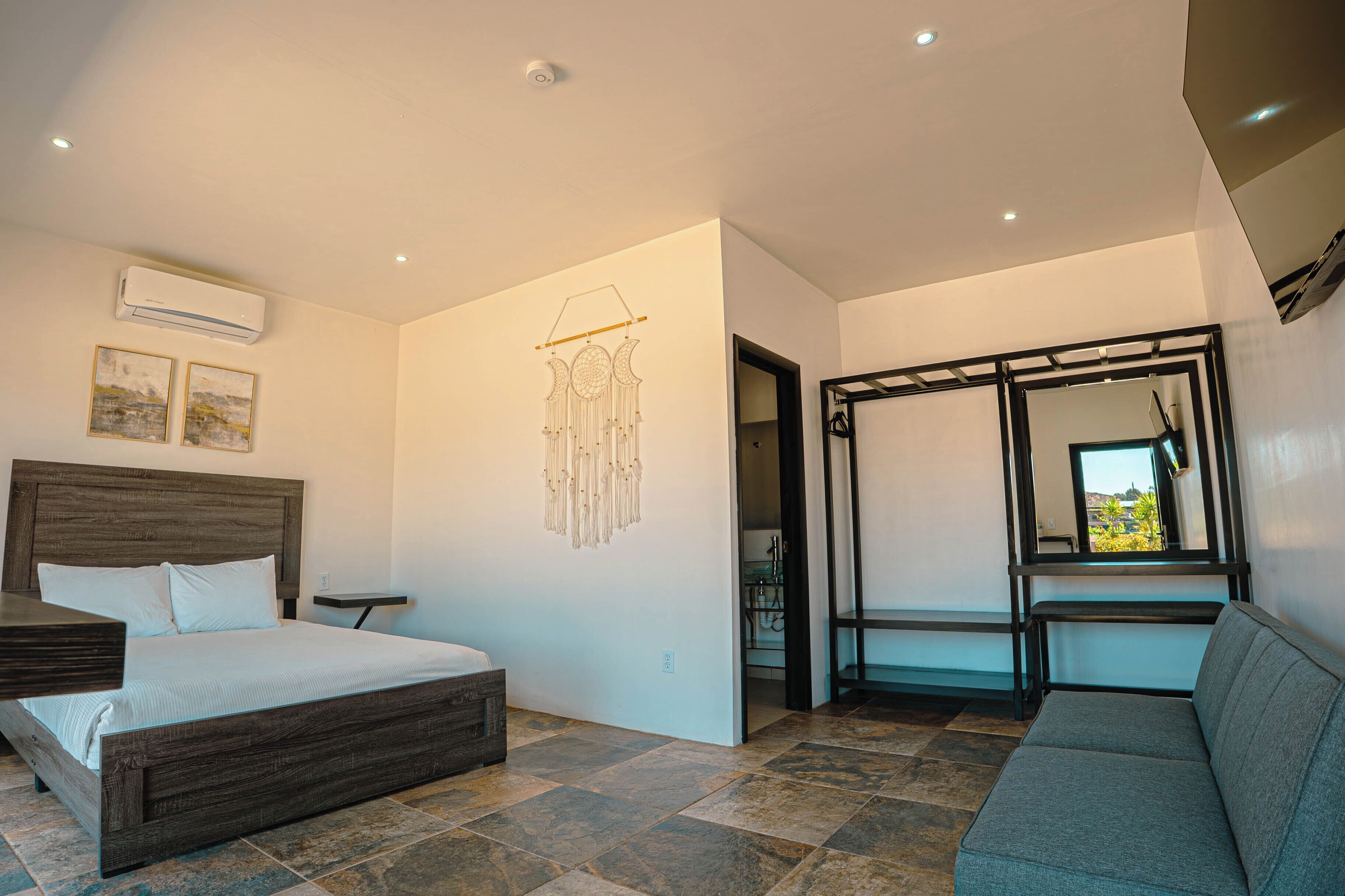 A bedroom with a bed, bedside table, wall art, air conditioning unit, and a view through a window.