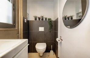 A small bathroom with a toilet, a sink, a mirror, and several potted plants. - Impeccable 3-bed Apartment in Athens (Nea Ionia)