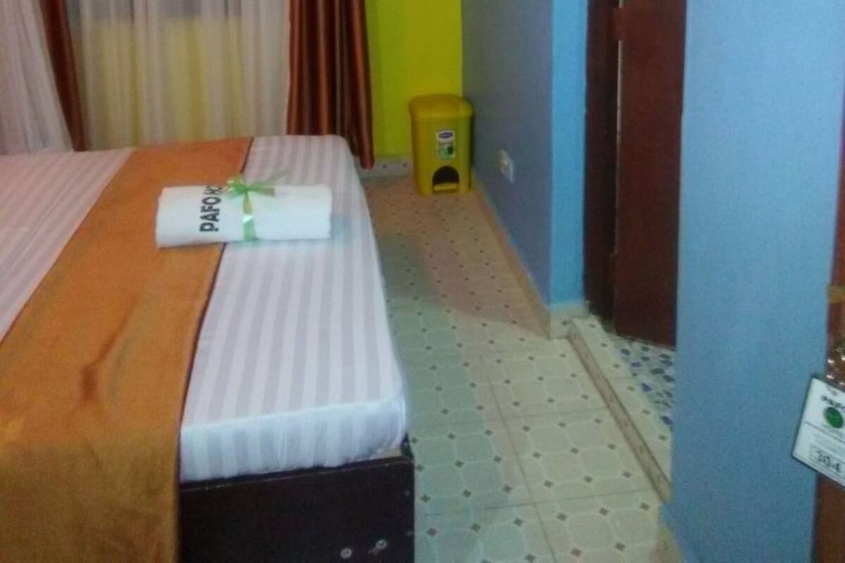 A hotel room with a bed, curtains, a small stool, and a door.