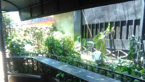 A covered outdoor area with a tiled floor, a metal railing, and lush greenery. - Pafo Hotel (Kisumu)