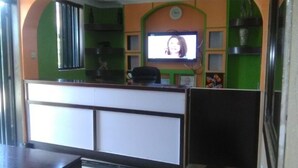 A room with a reception desk, a television mounted on the wall, and a seating area with a table and chairs. - Pafo Hotel (Kisumu)