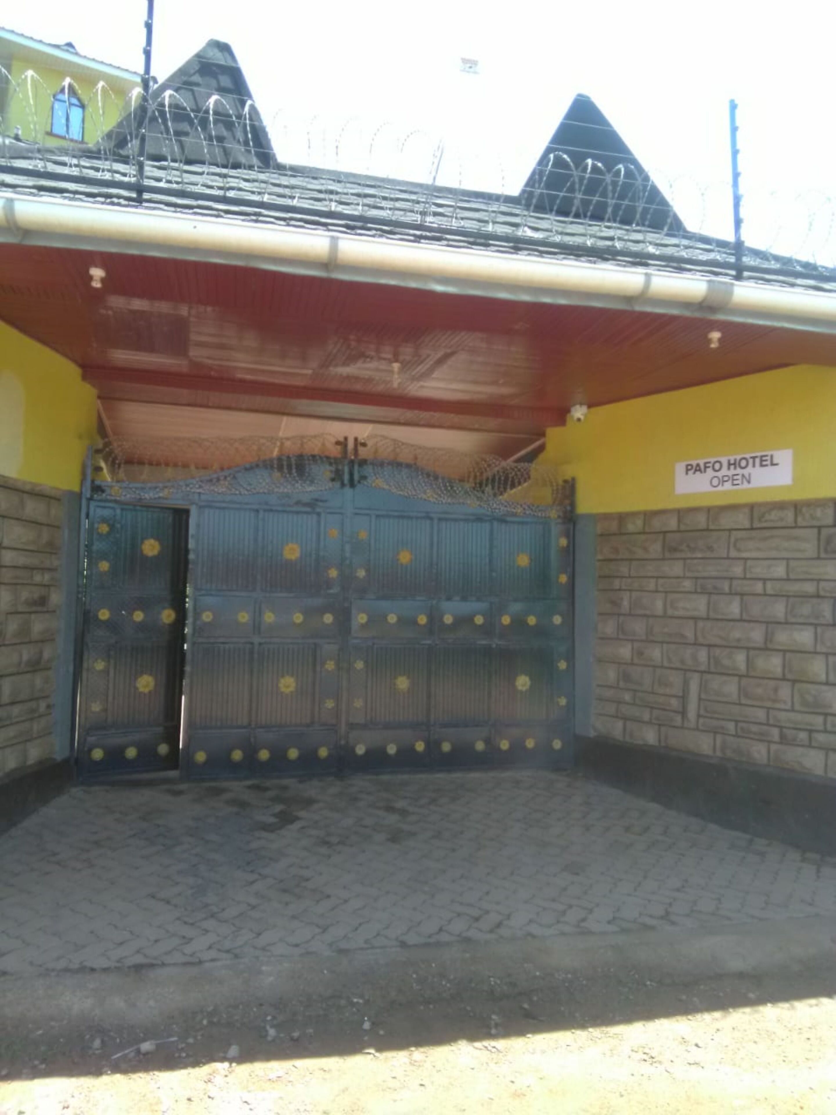 A PAFO HOTEL with a closed blue gate, a brick wall, and a yellow building in the background.