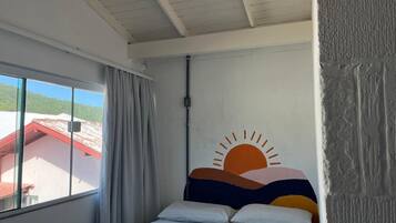 A bedroom with a bed, a window with curtains, and a wall with a sun design.