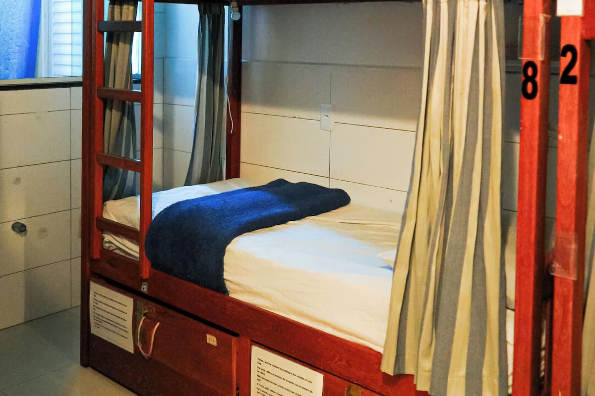 Una litera con escalera, cortinas y ventana con persianas.