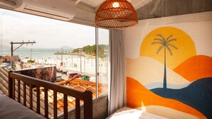 Una habitación con vista a la playa, una hamaca, un cuadro de una palmera y una lámpara colgante.