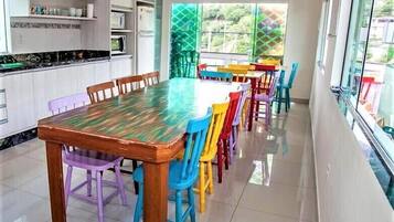 A dining area with a wooden table and colorful chairs, a kitchen with white cabinets, and a view through large windows.