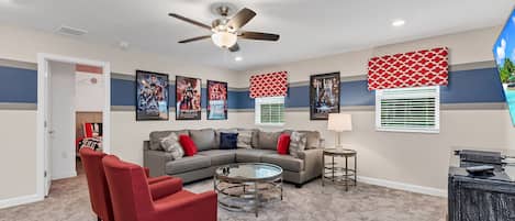 A living room with a sectional sofa, red chairs, a coffee table, and a ceiling fan.