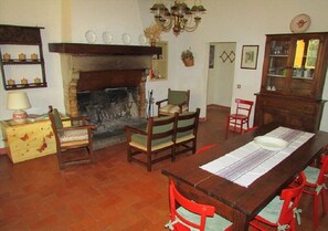 A traditional living room with a fireplace, wooden furniture, and a dining table set for four. - Agriturismo Dea- Volta (Valfabbrica)
