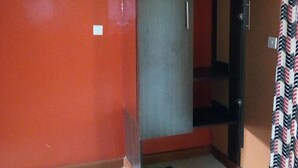 Una habitación con una pared roja, un armario gris, suelo de baldosas y una cortina estampada.