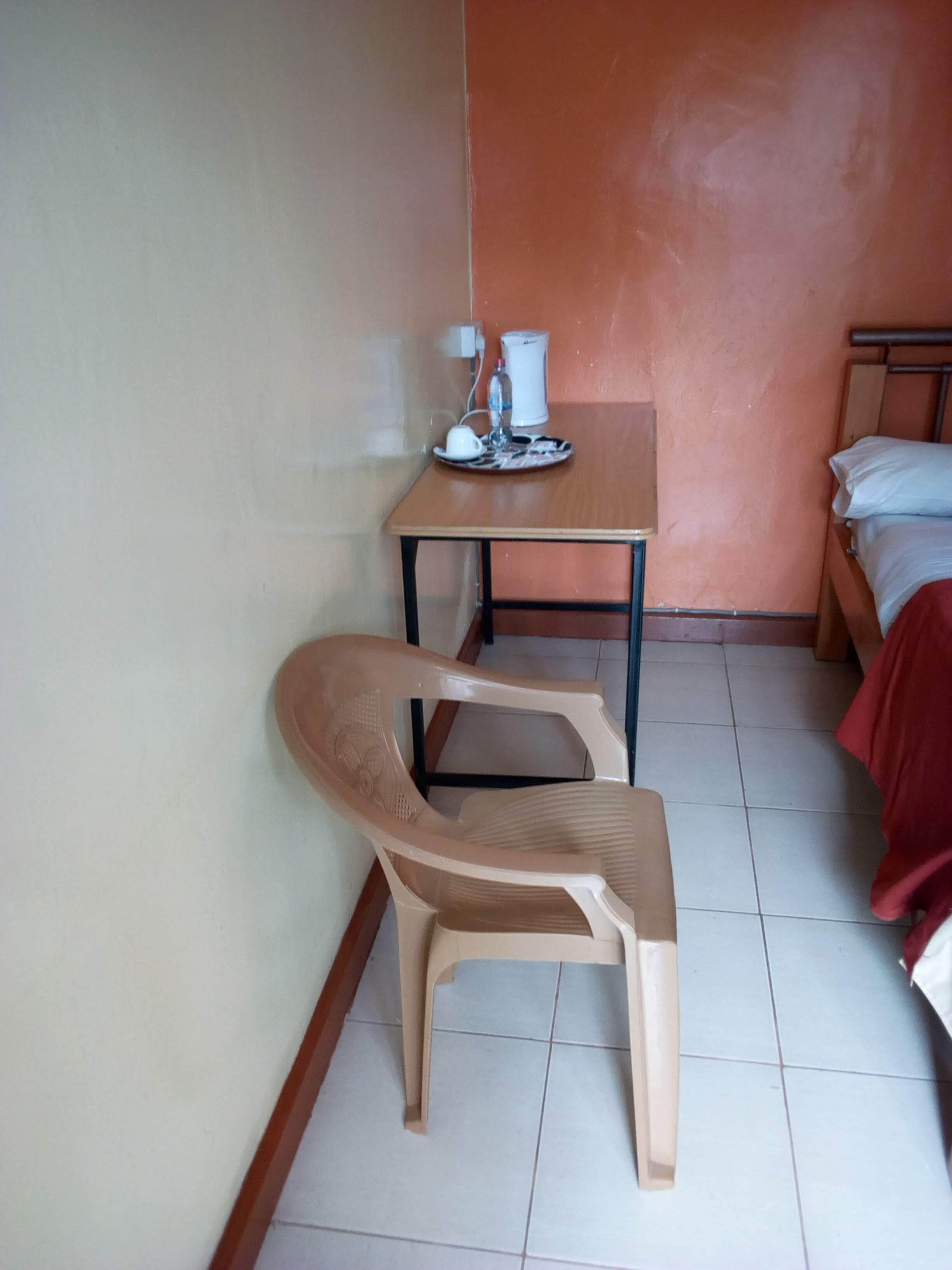 Ein kleines Zimmer mit einem Einzelbett, einem Tisch mit Wasserkocher und Tassen sowie einem Plastikstuhl.