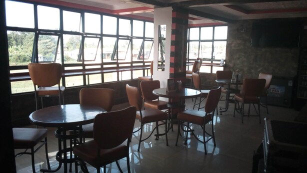 A cafe with multiple tables and chairs, large windows with a view of greenery, and a tiled floor. - The Baron Hotel (Thika)