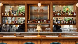 Un coin bar avec des étagères en bois remplies de différentes bouteilles d’alcool, un tableau accroché au-dessus des étagères et une caisse enregistreuse.