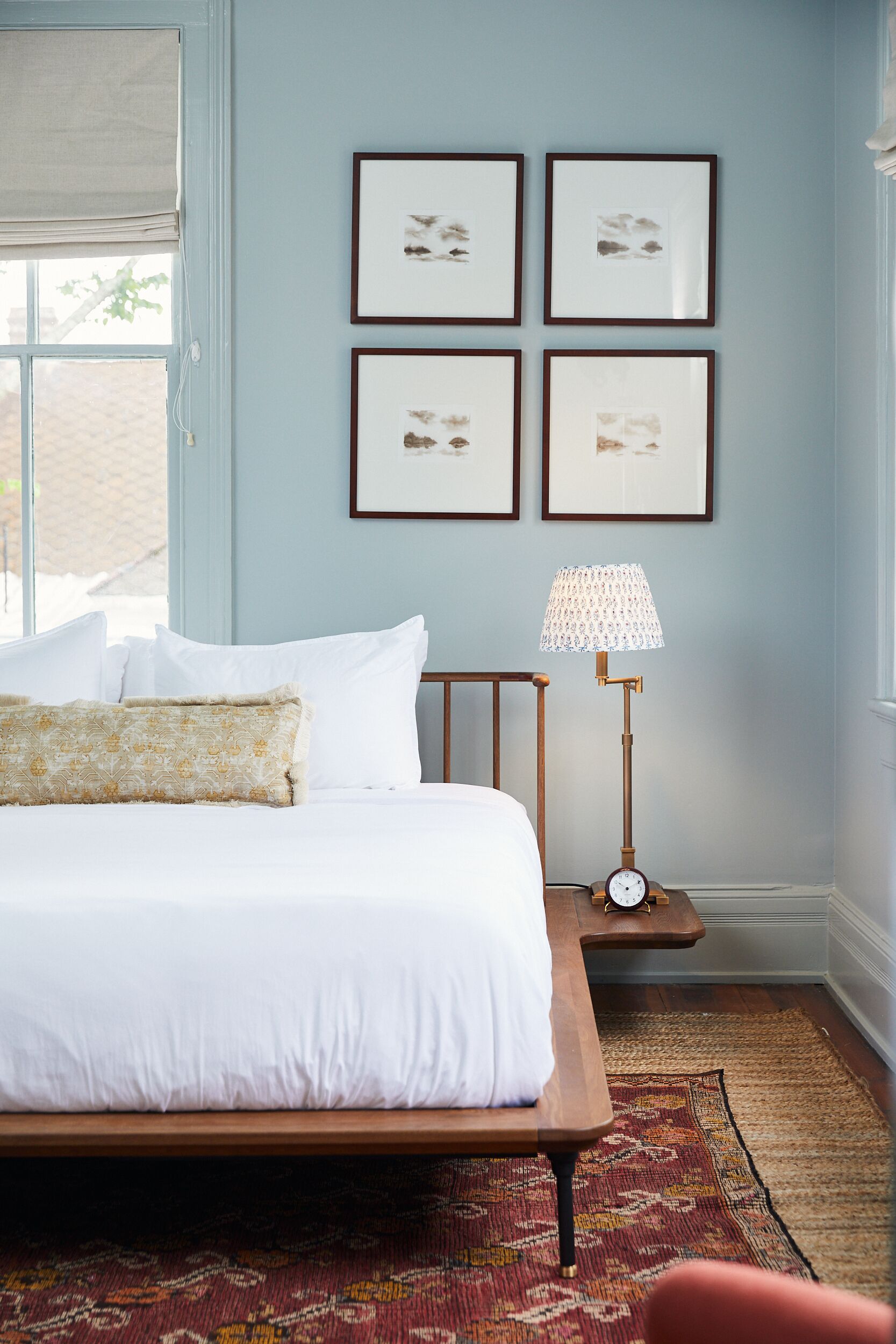 A neatly made bed with white linens and decorative pillows, a bedside table with a lamp, and framed artwork on the wall.