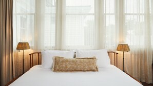 Une chambre d’hôtel avec un grand lit, deux lampes de chevet, des rideaux légers et un coussin décoratif à motifs.